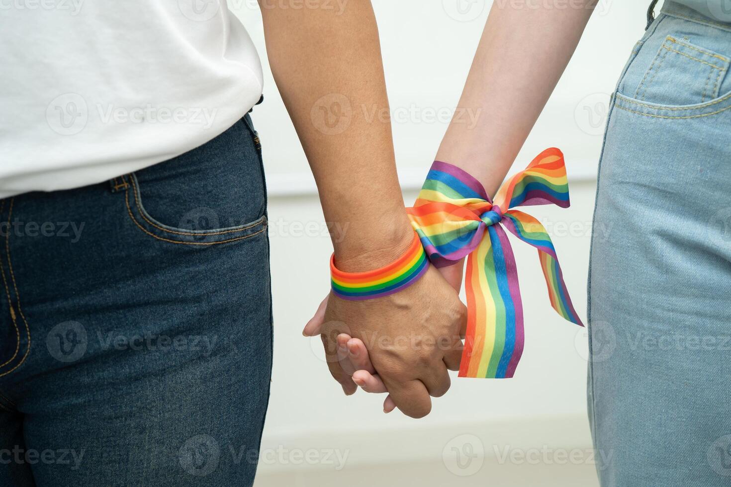Asian LGBT couple woman holding hand wearing rainbow wristband. photo