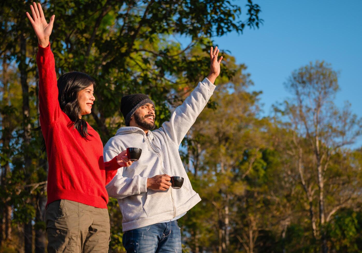 man and woman are standing in a park, holding cups and smiling photo