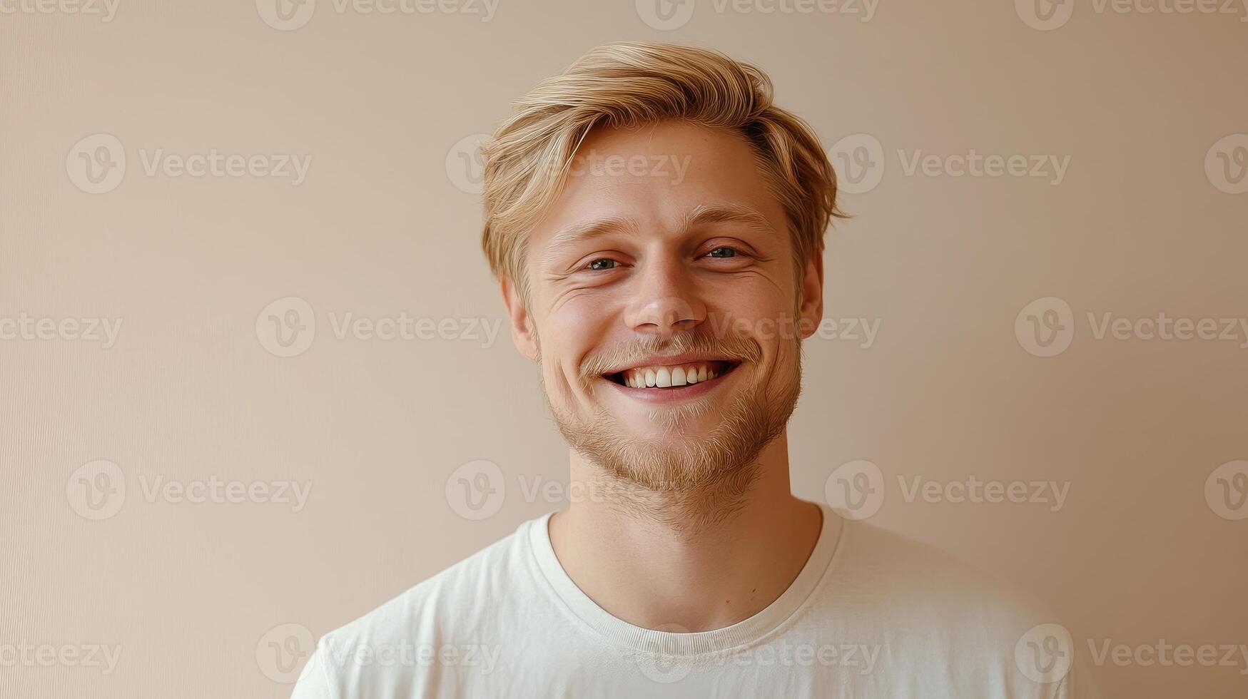 Smiling young man with blonde hair poses against a light background during a cheerful indoor moment photo