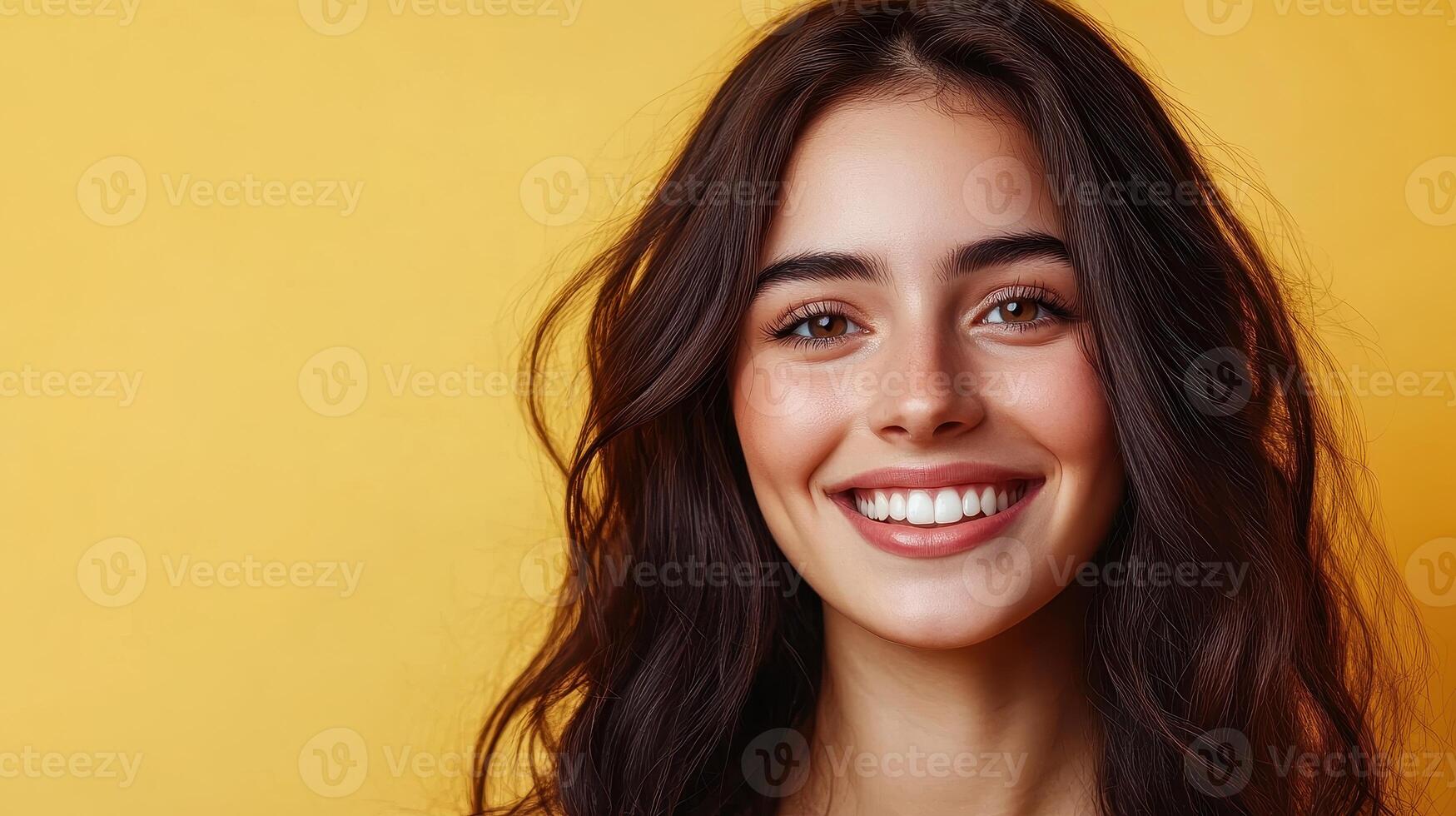 Happy young woman smiles brightly against a vibrant yellow background showcasing her joyful expression and glowing skin in an indoor setting photo