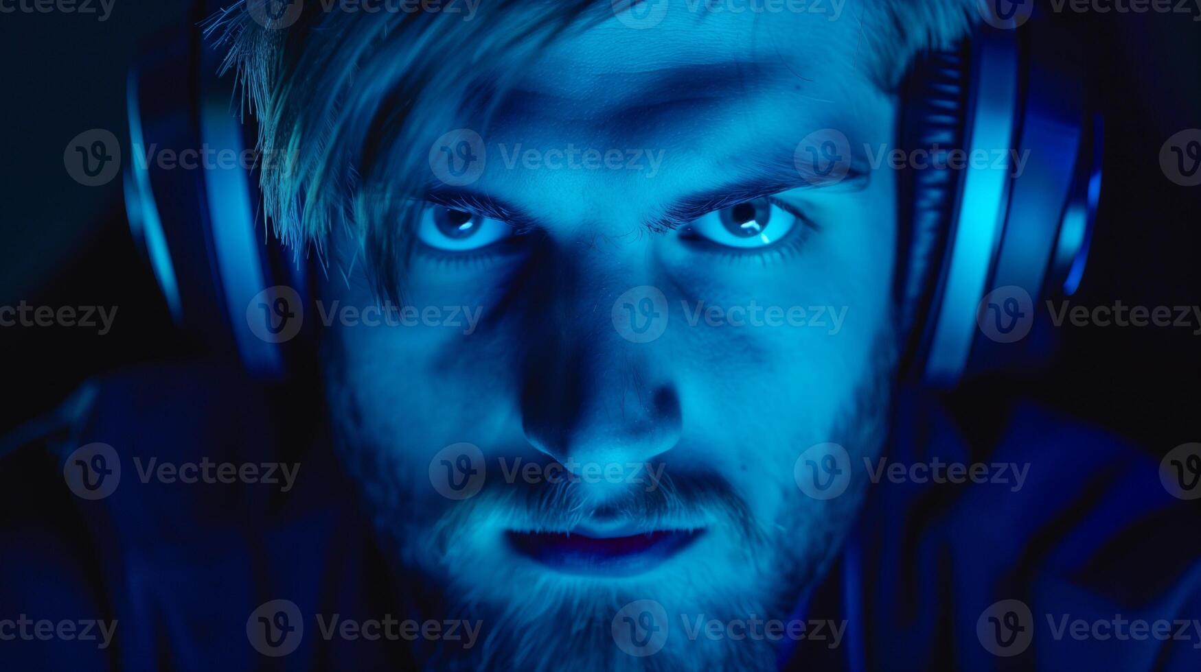 Intense esports competitor face under dramatic blue light image closeup. Bearded man pro gamer wearing headphones close-up photography. Gaming tournament concept photo realistic