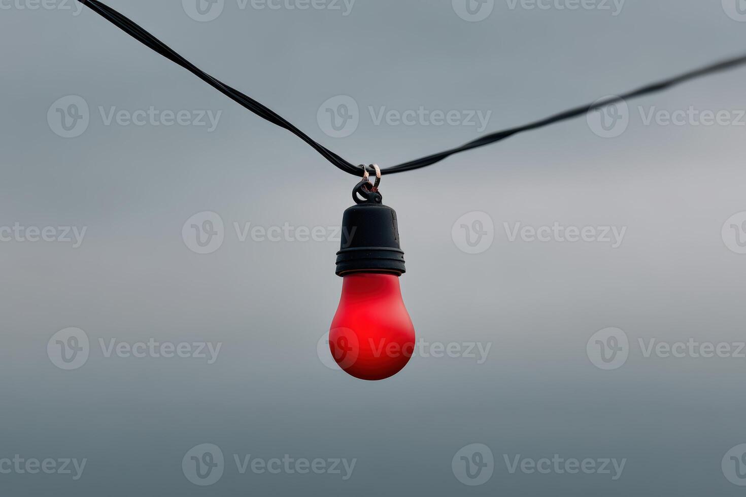 Glowing red light bulb hanging against a cloudy sky illuminating the dark atmosphere photo