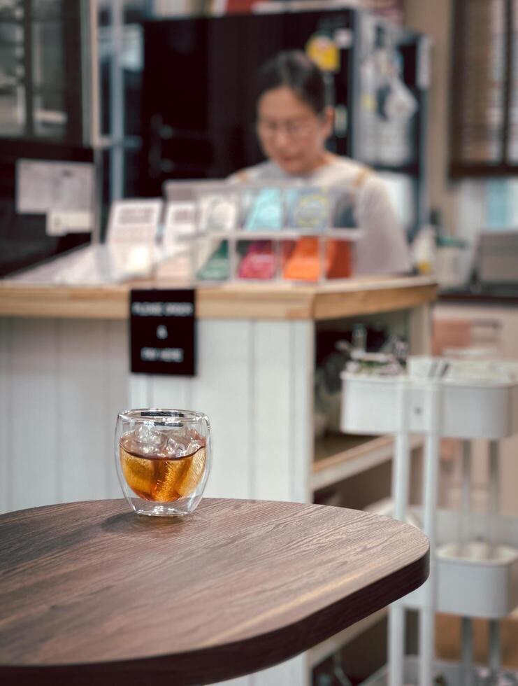 Iced coffee on table in cafe with blurred woman in background. photo