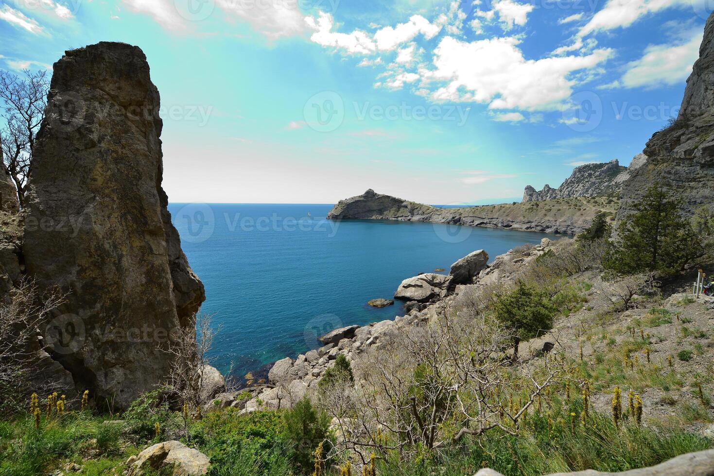 A cliff over a water body with a large rock in front photo