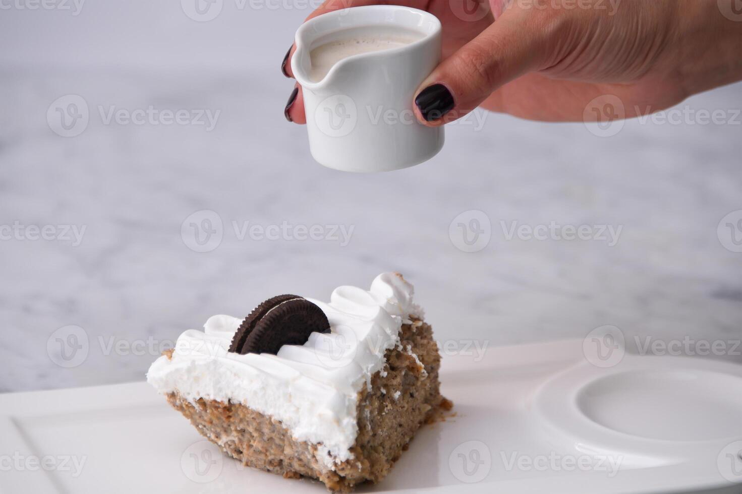 Oreo Cream Cake Slice with crushed chocolate sandwich cookies baked topped with whipped cream with dripping milk sauce served in plate isolated on background closeup top view of indulgent dessert photo