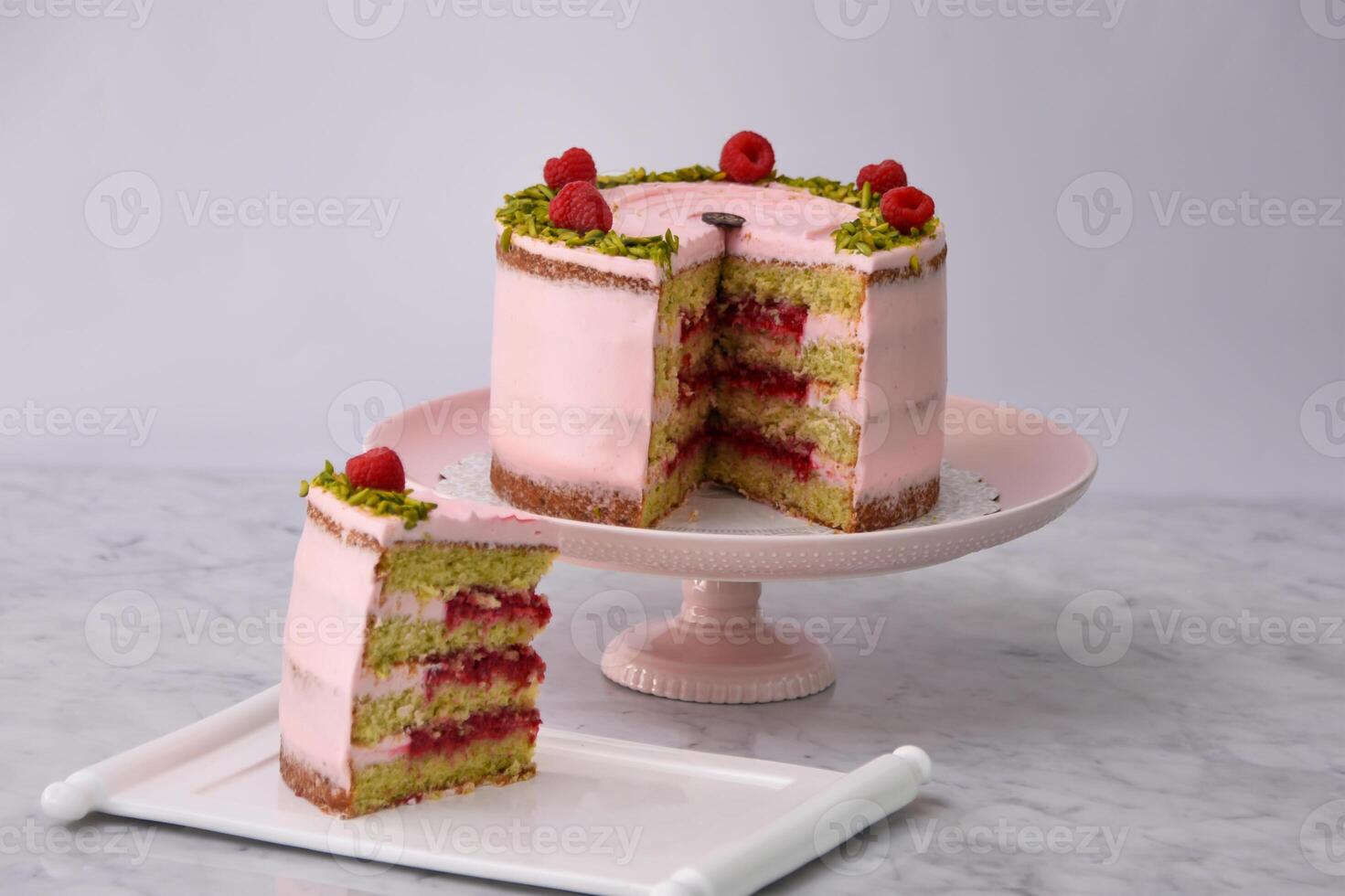 Elegant Raspberry Pistachio Layer Cake with Slice frosted with light pink cream and garnished with fresh raspberries and chopped pistachios closeup side view of cafe dessert photo
