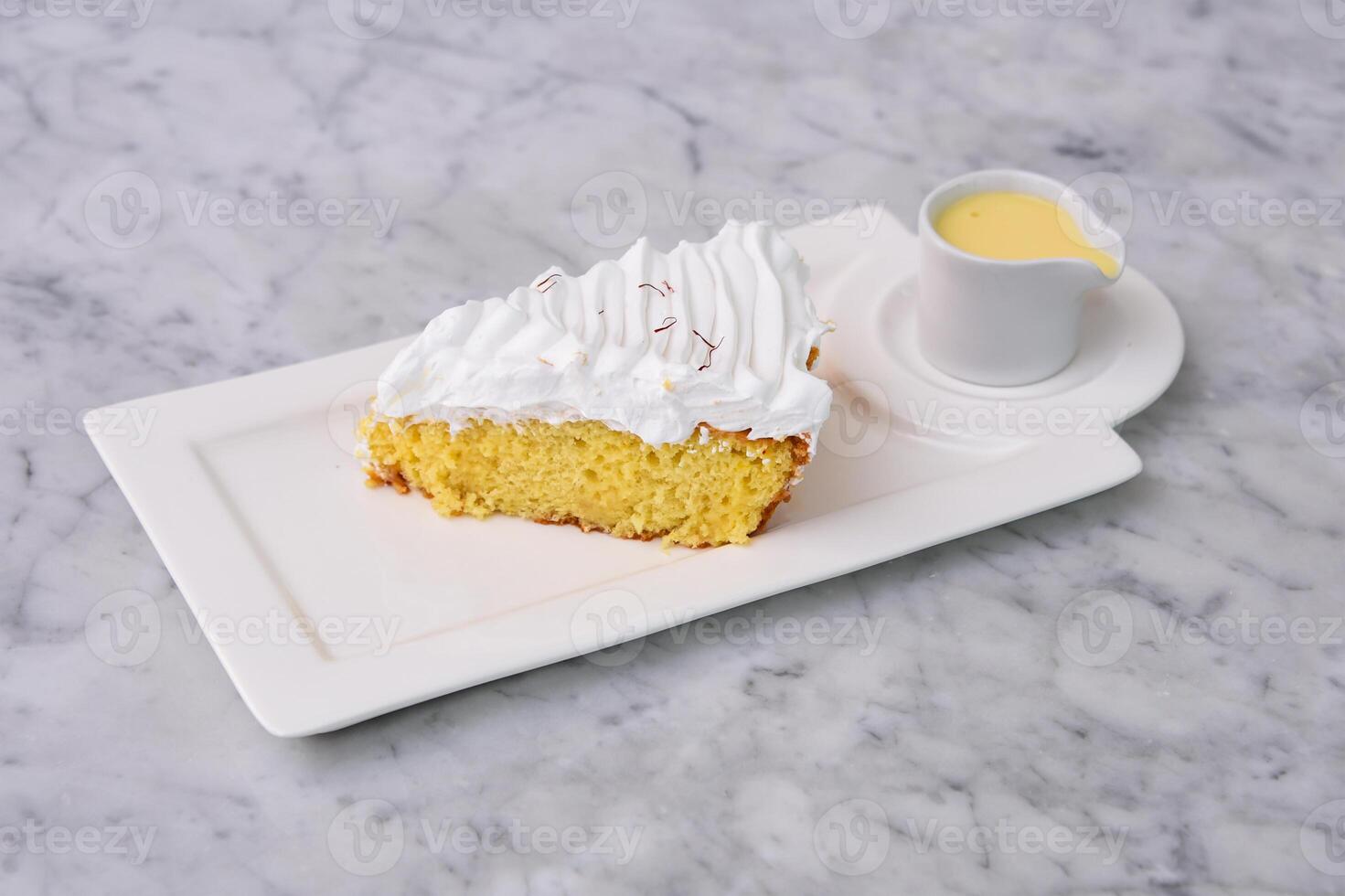 Tres Leches cake Slice with small bowl of extra milk sauce served in tray topped with fluffy whipped cream and saffron threads side view of indulgent dessert photo