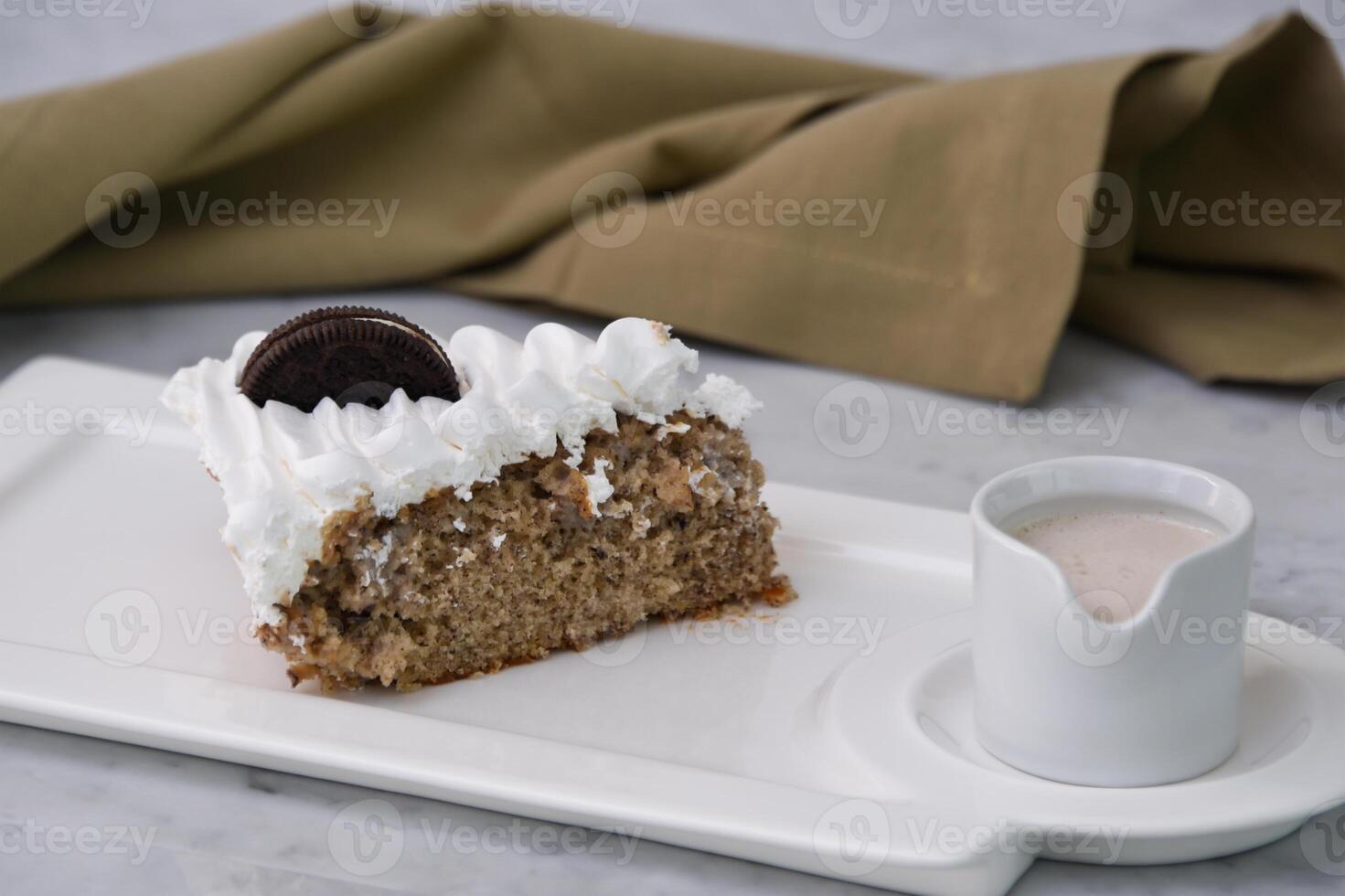 Oreo Cream Cake Slice with crushed chocolate sandwich cookies baked topped with whipped cream with milk sauce served in plate with napkin isolated on background side view of indulgent dessert photo
