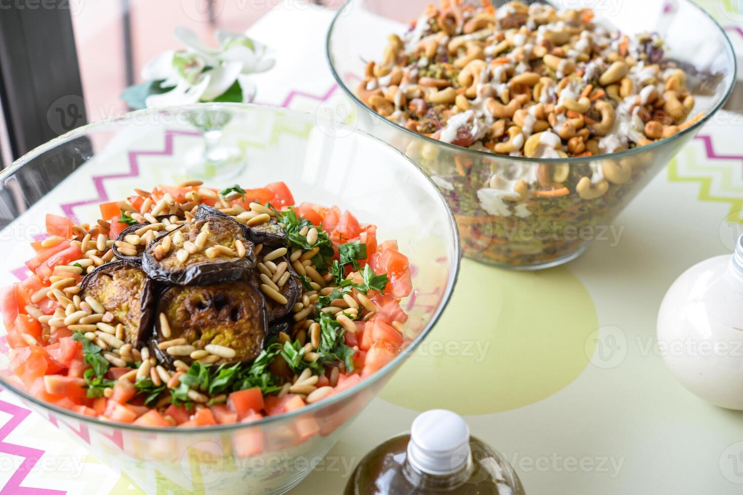 Assorted Salads in Glass Bowls include grains, vegetables, and nuts served on a table with dressing bottles closeup side view photo