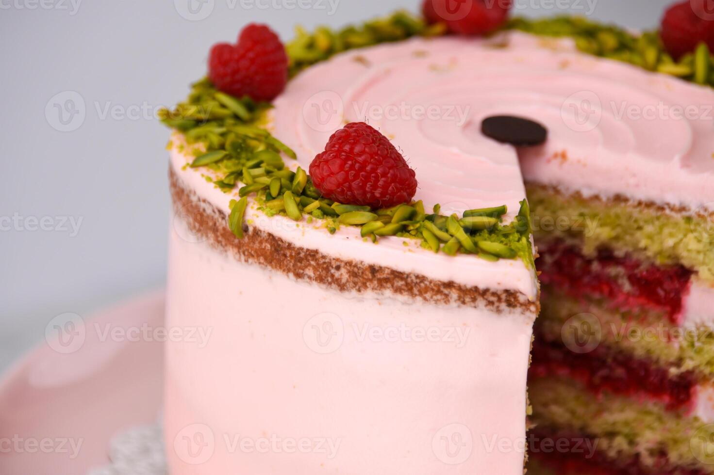 layered Raspberry Pistachio Cake frosted with light pink cream and garnished with fresh raspberries and chopped pistachios closeup side view of cafe delicious dessert photo