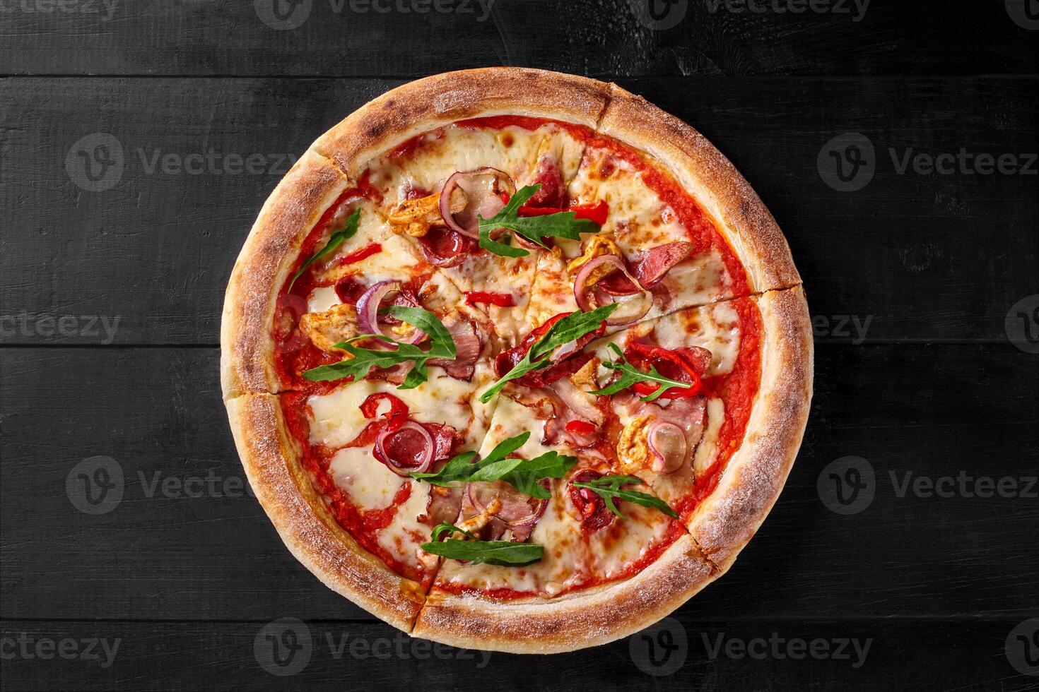 Delicious pizza with chicken, bacon, arugula and mozzarella on black wooden table photo