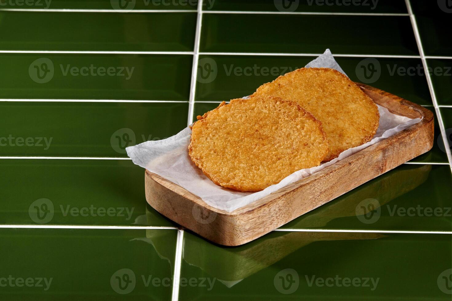 Two chicken or fish patties resting on wooden tray with parchment paper on green tile photo