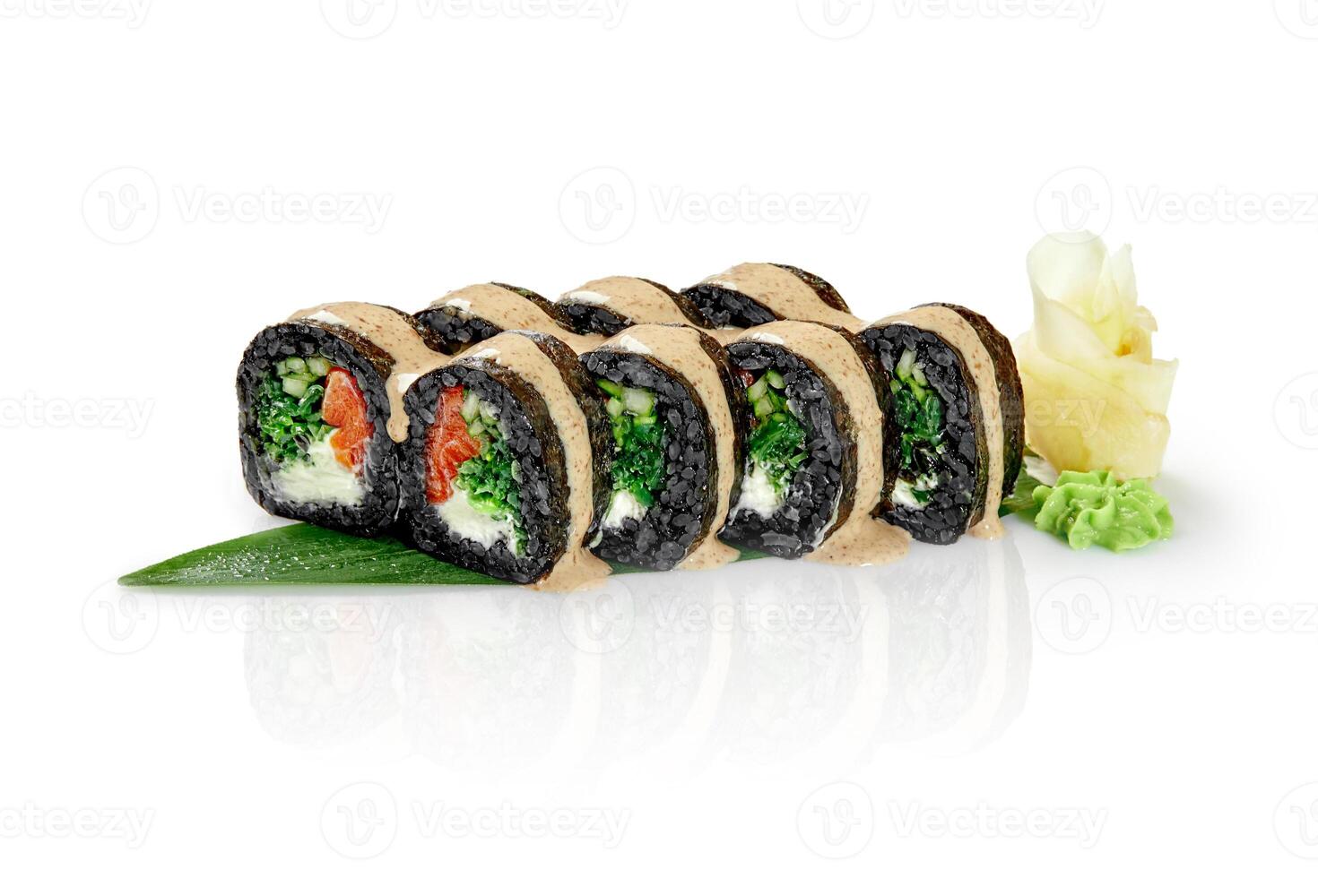 Black sushi rolls with salmon, vegetables and cream cheese drizzled with sauce on a green leaf photo