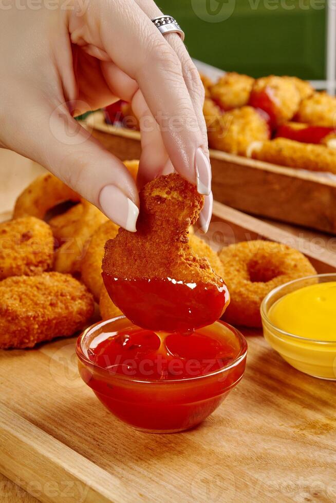 Woman dipping chicken nuggets in red sauce with various nuggets and sauces photo