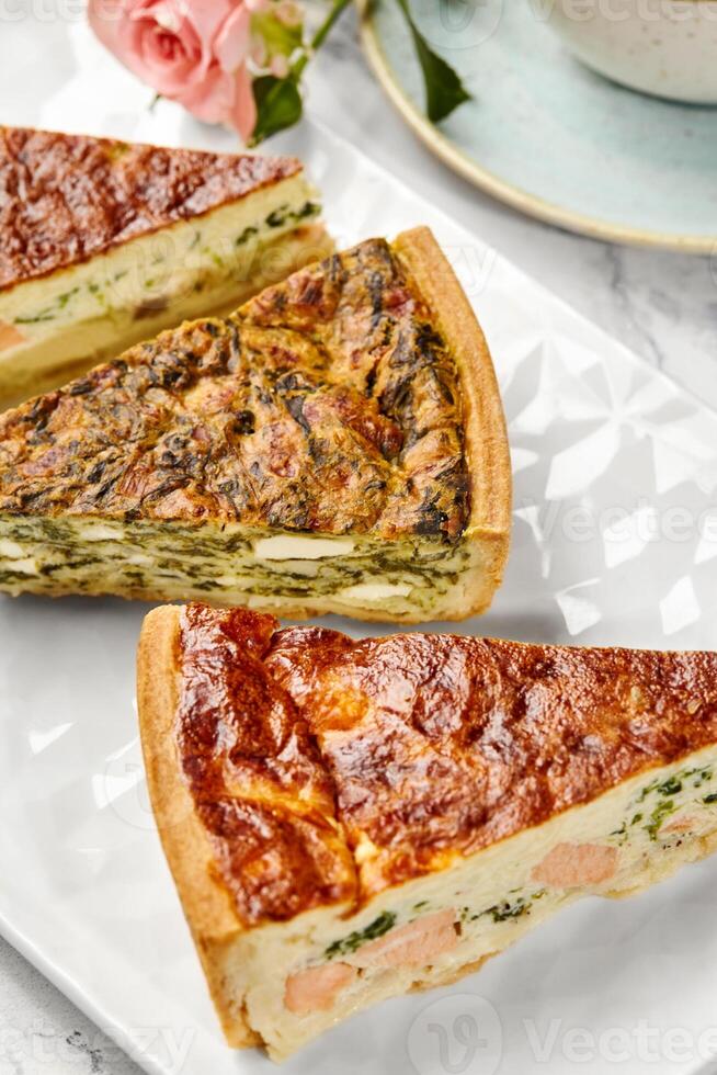 Delicious homemade quiches with salmon, spinach and mushrooms filling resting on white plate photo