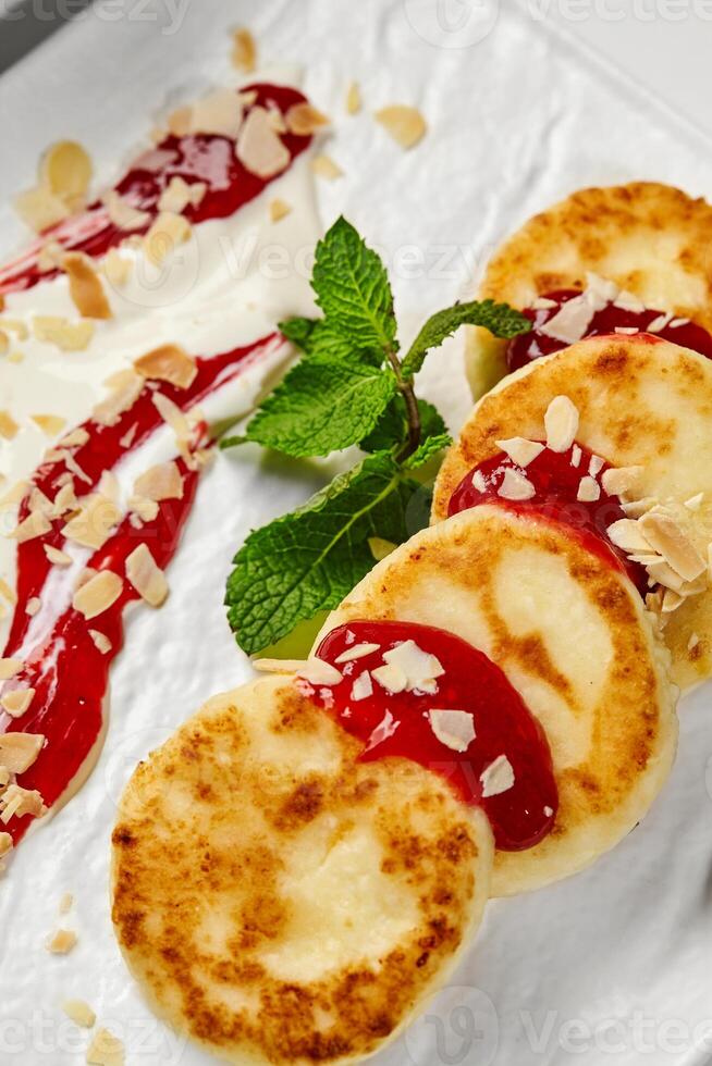 Syrniki with raspberry jam, almond flakes, sour cream and mint on white plate photo