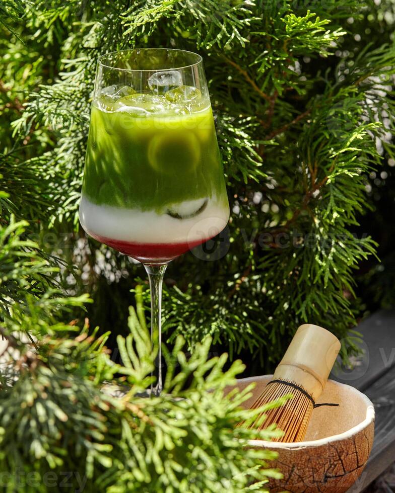 Iced matcha latte with coconut milk presented in wine glass with chasen on blurred green background photo