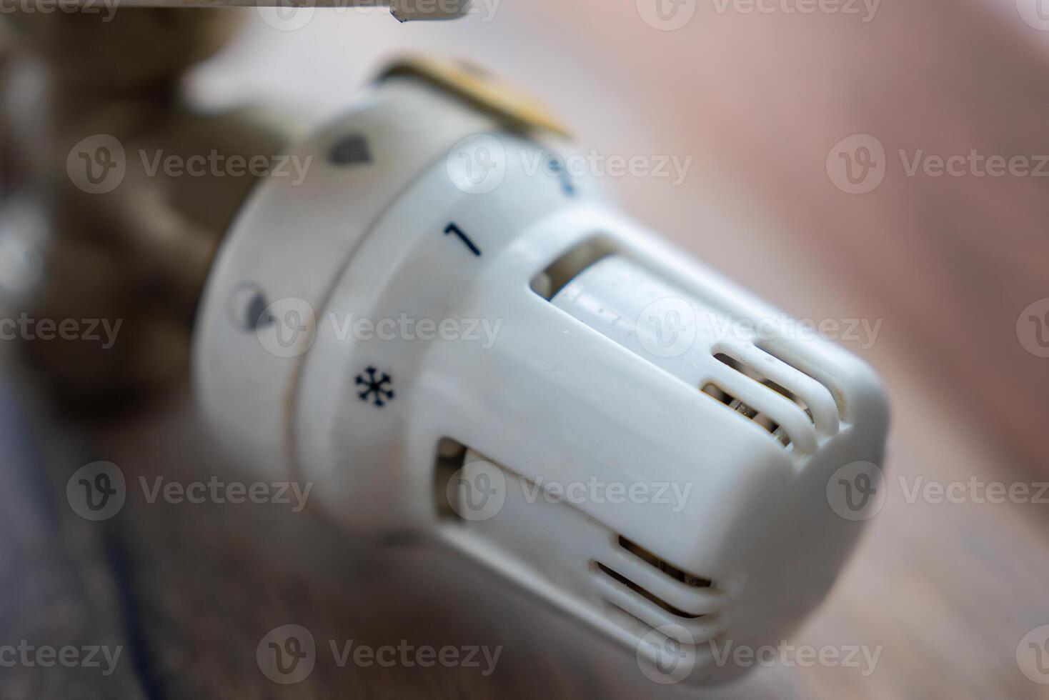 Close up view of a white rotary heating knob with numbered settings and a snowflake icon, likely part of a water or heating control system. Blurred wooden background. photo