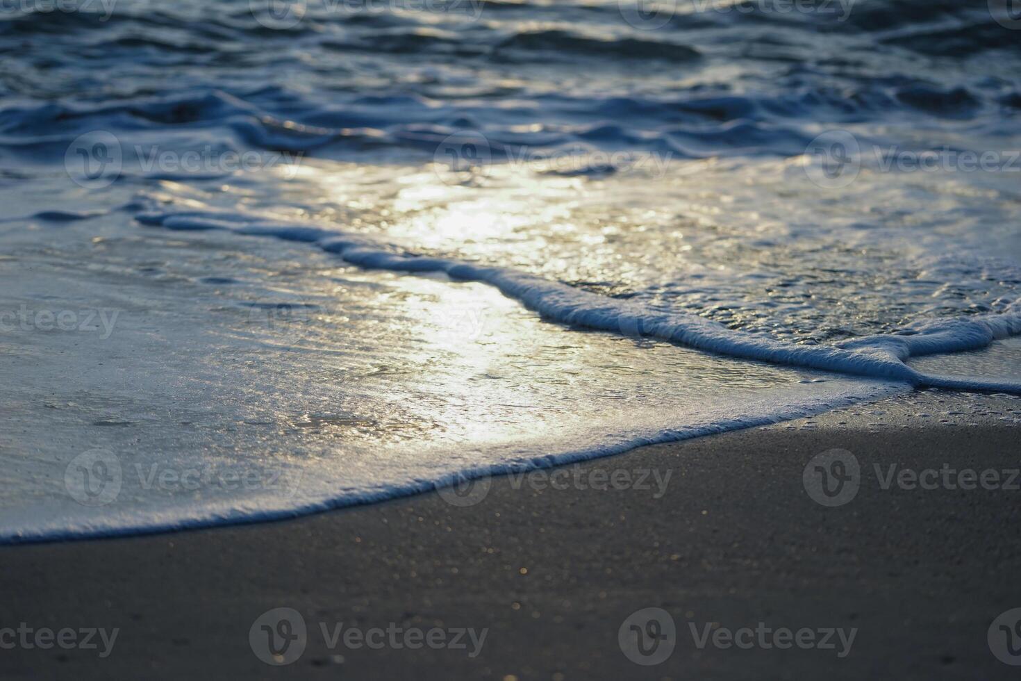 Closeup wave sufing on the sand beach with reflection of the sun light on the surface of the water photo