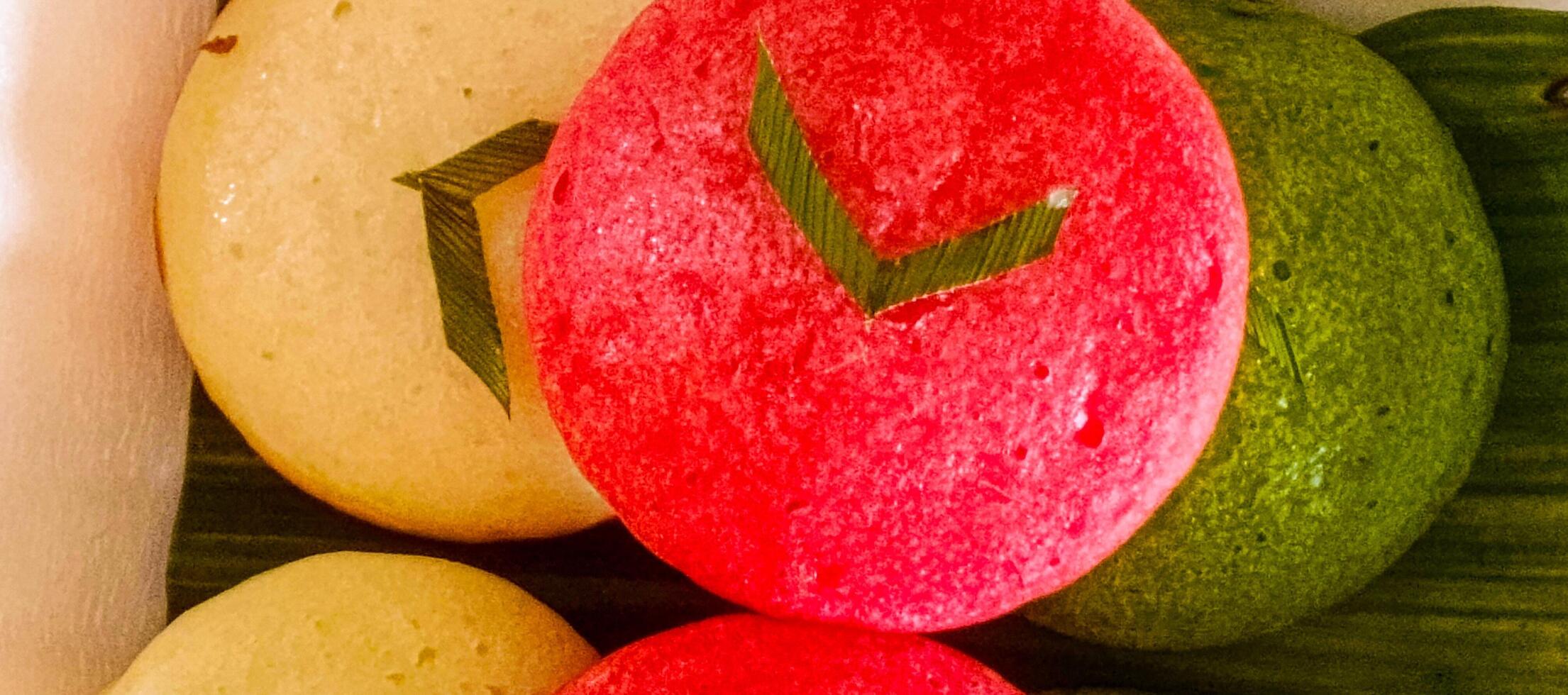 Close-up of traditional Indonesian apem, soft and fluffy steamed rice cakes in red, green, and white, decorated with pandan leaves photo