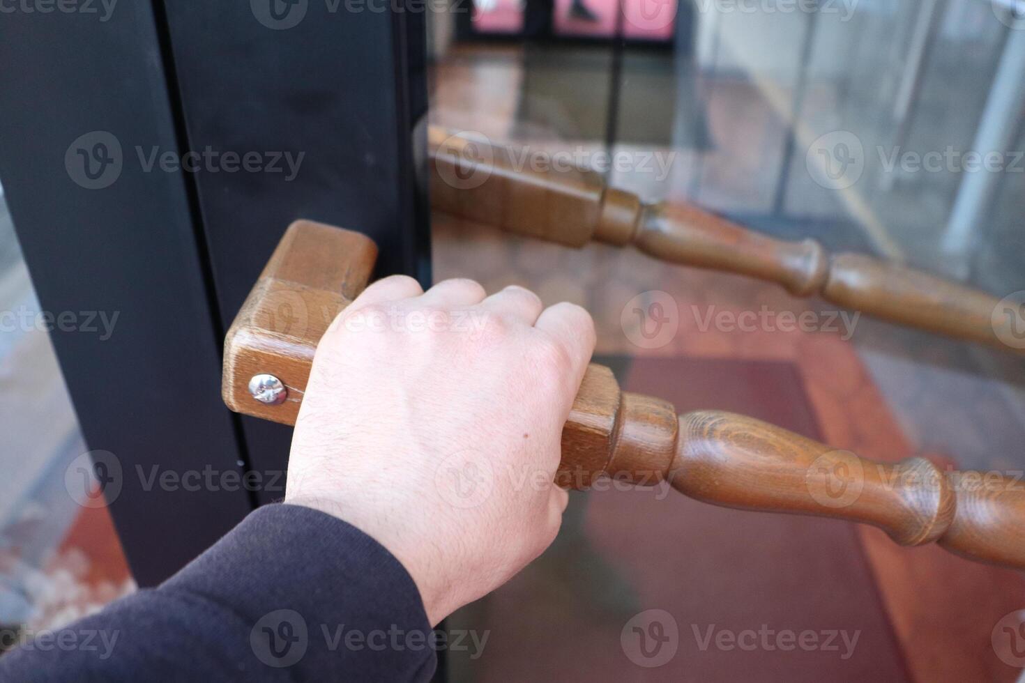 A hand grasping the wooden handle of a door to open a modern entrance to a building photo
