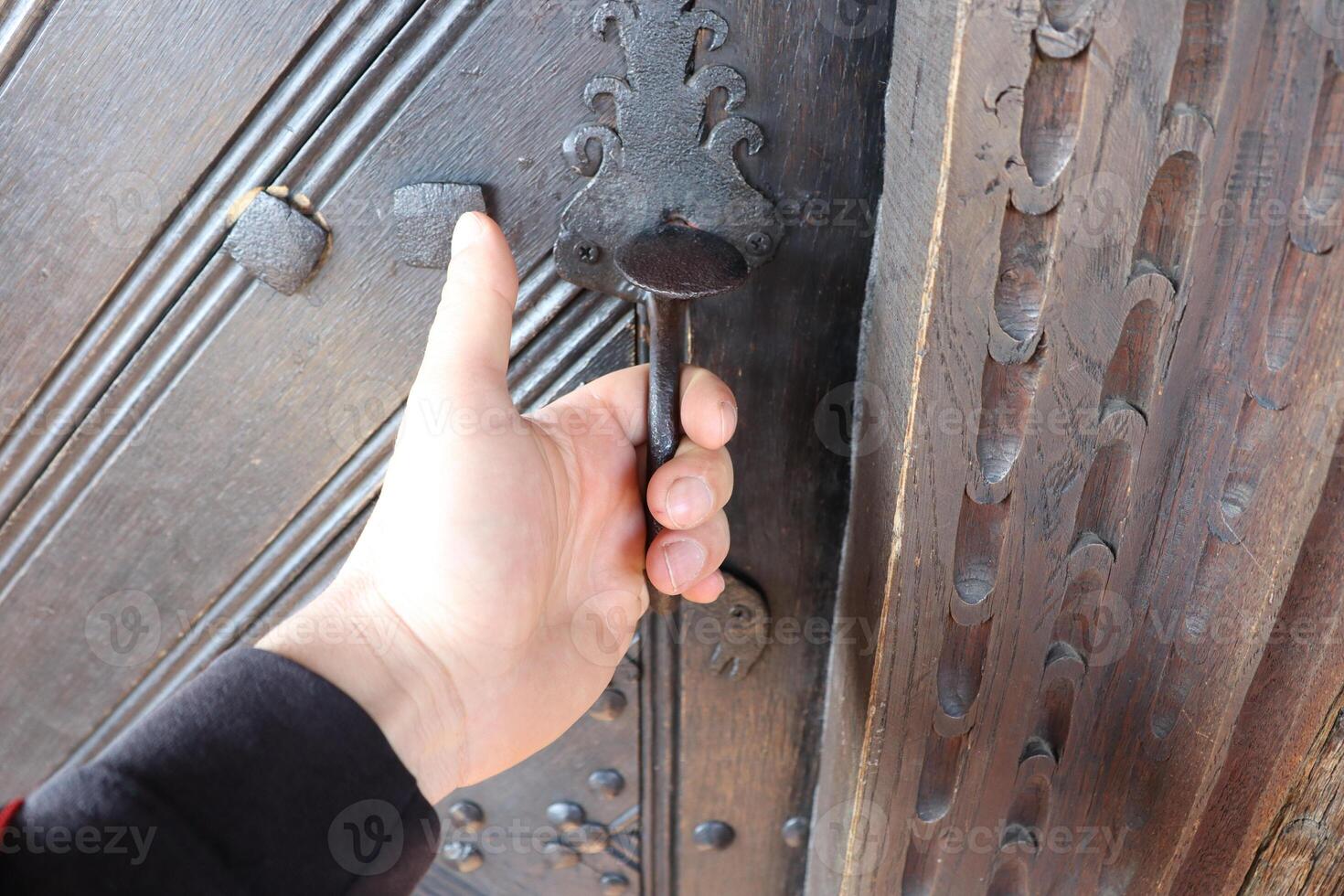 A hand grips an ornate door handle, highlighting its intricate artwork and elaborate design photo