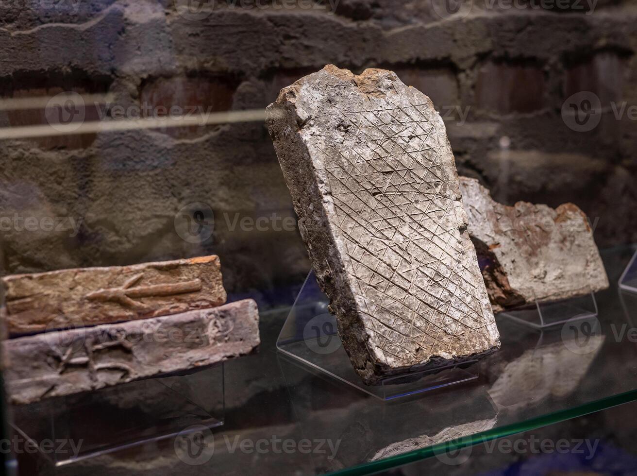An old stone slab is on display in a glass case photo