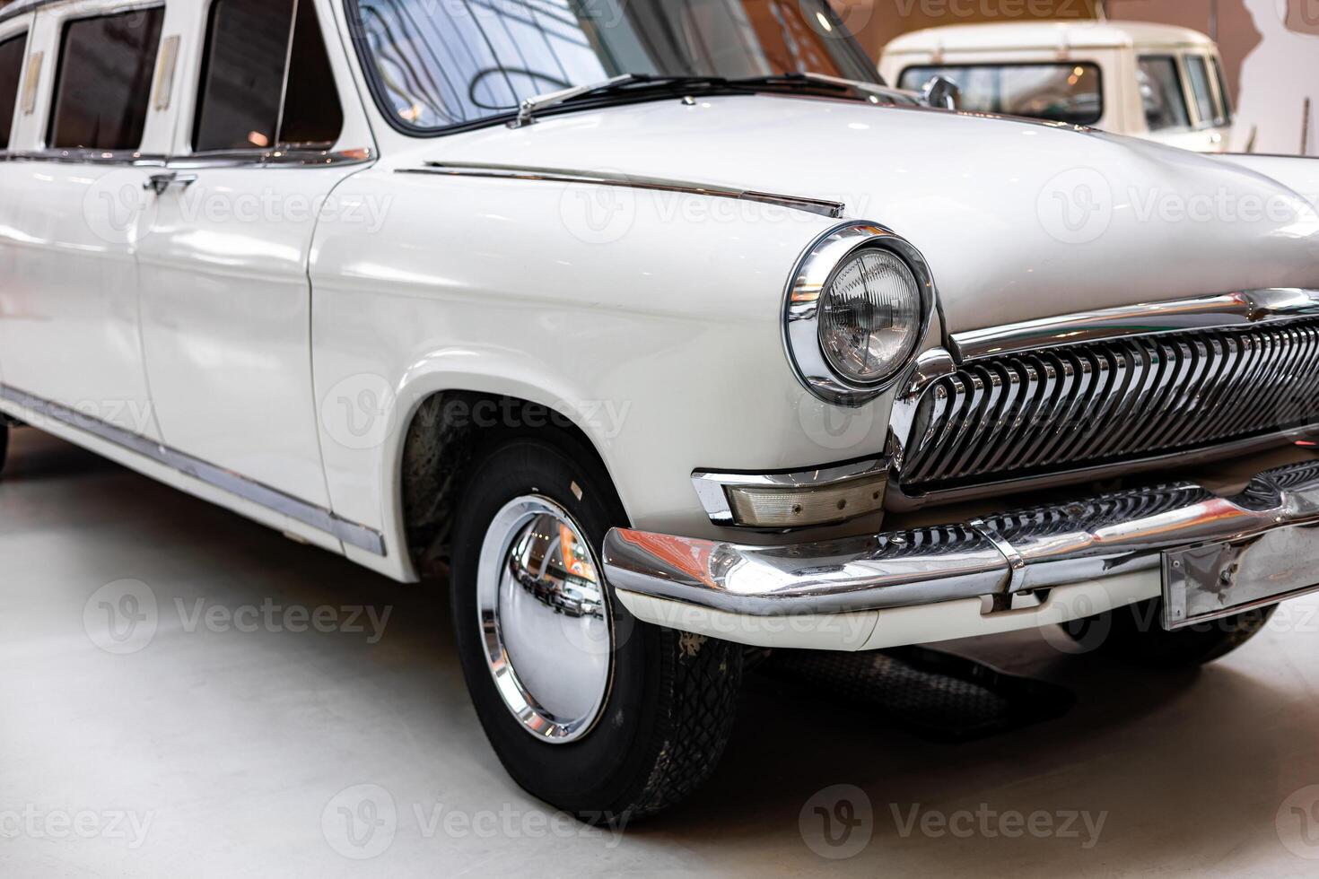 An old white car is parked in a museum photo