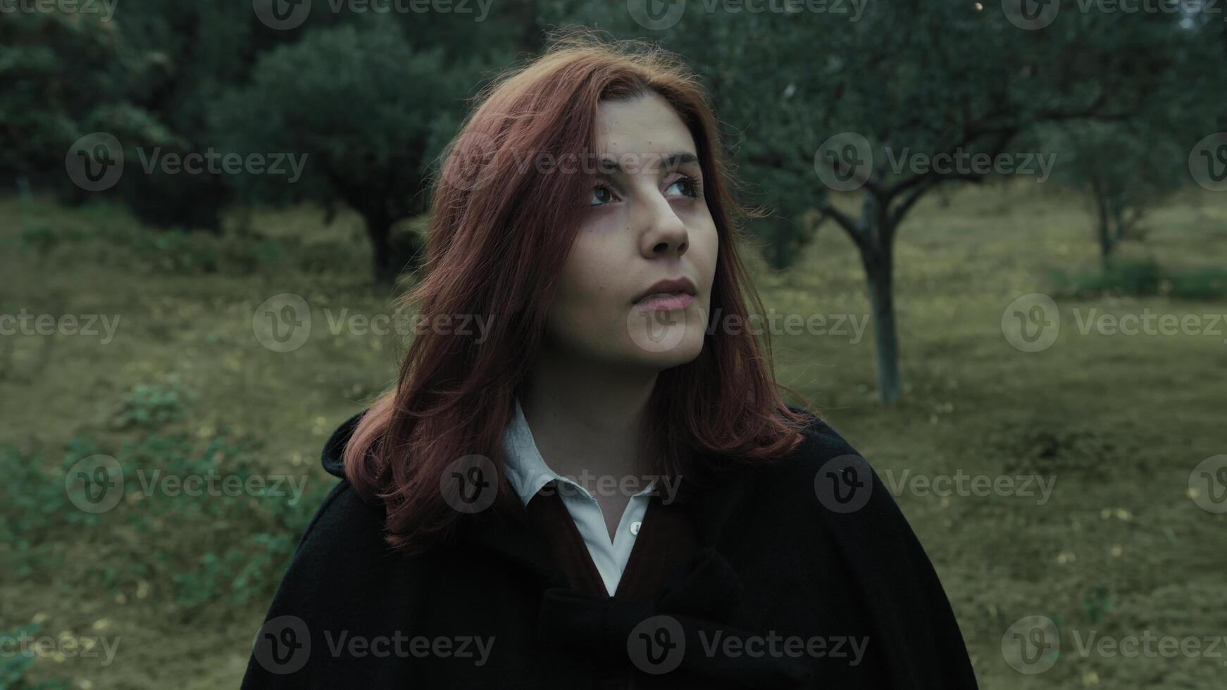 Young Woman With Red Hair Looks Around In A Public Park In Cloudy Cold photo