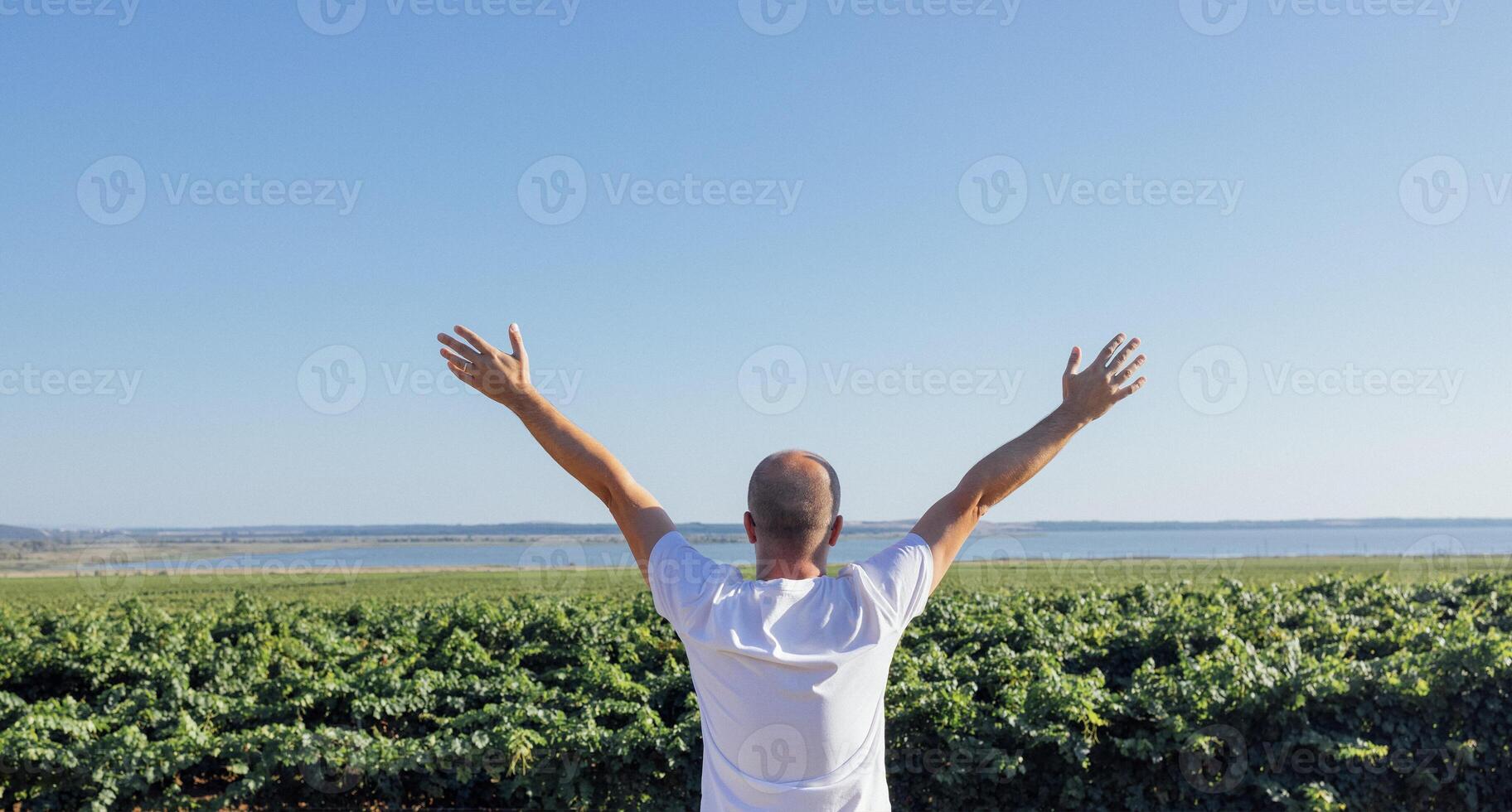 A young man in a white T-shirt spreads his arms and looks at the sea coast. A middle-aged male stands with his back and enjoys the natural scenery. photo