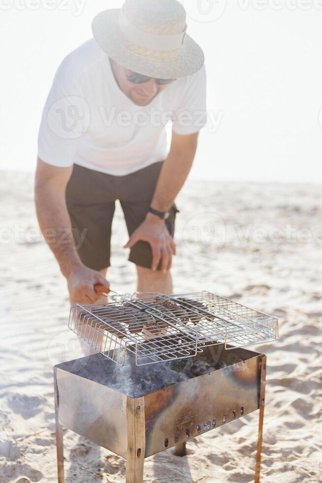 A young man in a summer casual outfit is having a barbecue on the sandy beach photo