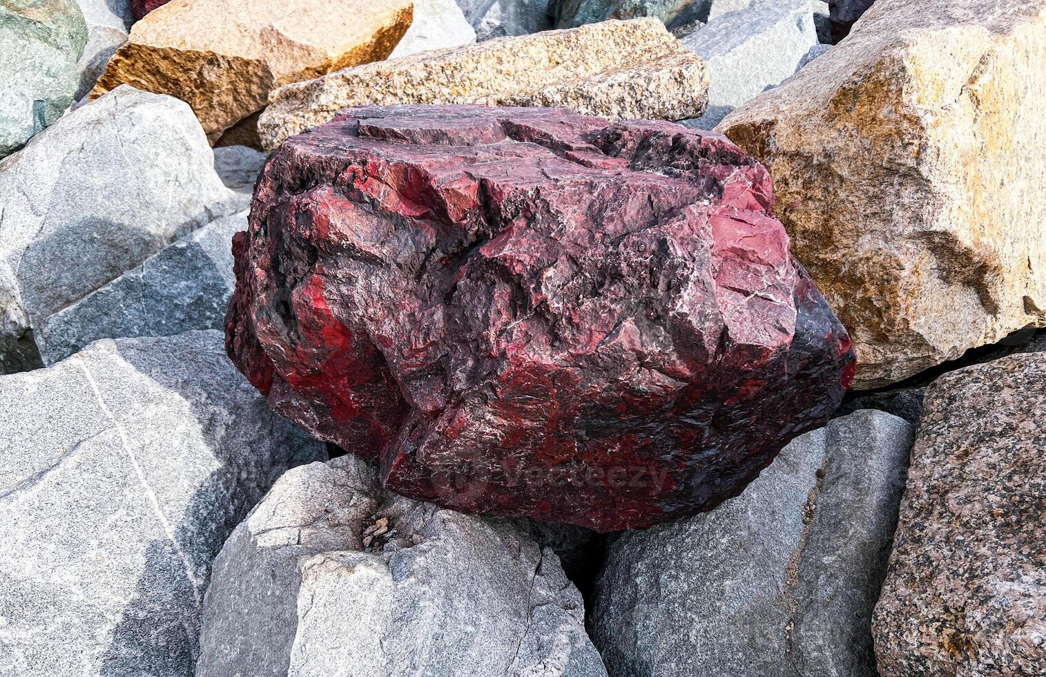 Striking red rock stands prominently among gray, brown boulders, natural variations in color and texture, geological background photo