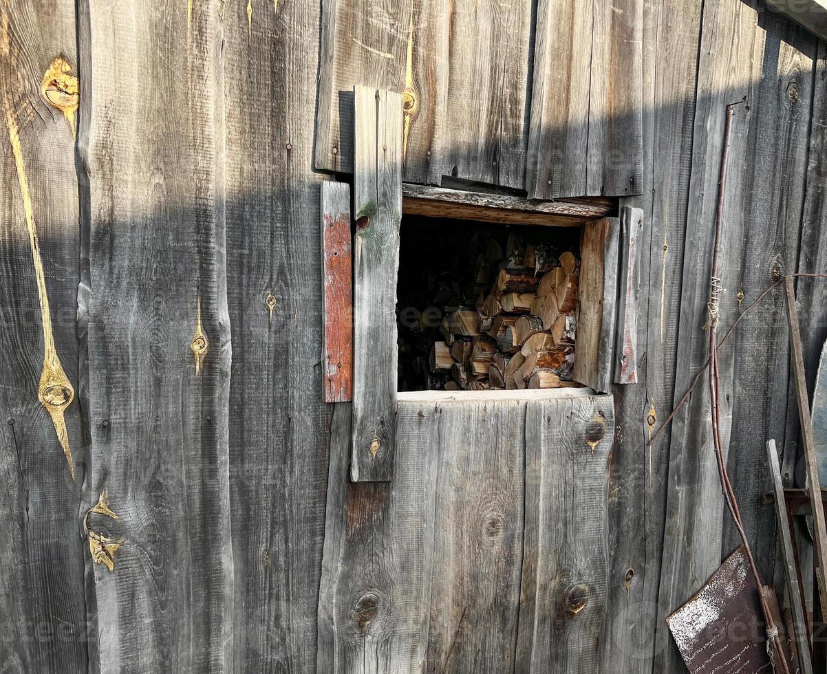 Weathered wooden cabin wall features a small rectangular window filled with neatly stacked firewood. The rustic, aged wood texture , countryside ambiance photo