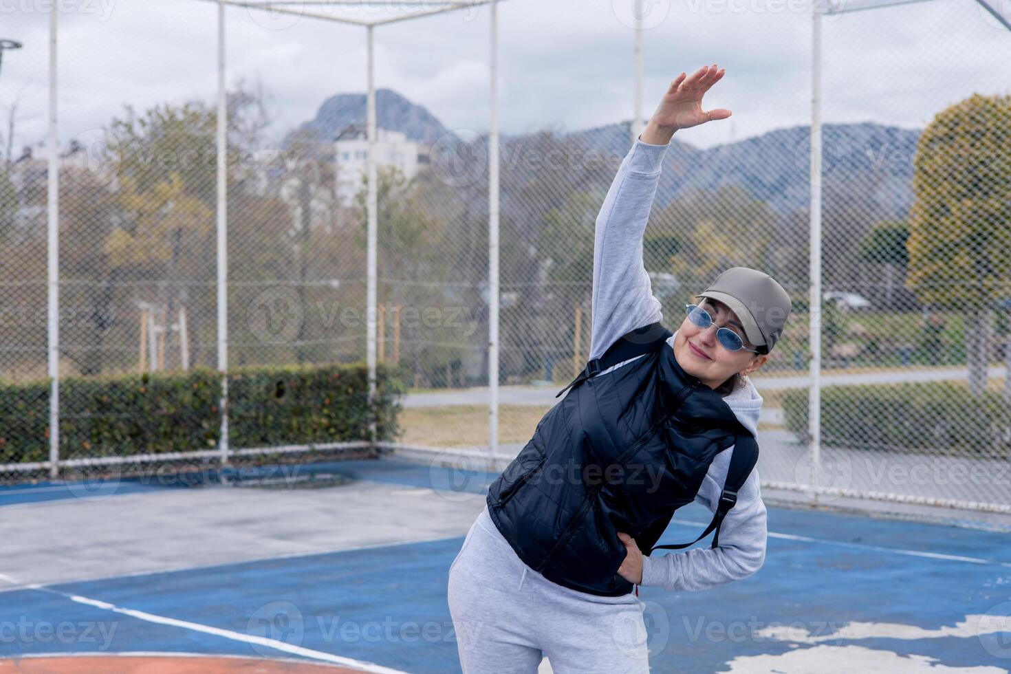 Woman stretching on basketball court in an urban park during cloudy afternoon photo