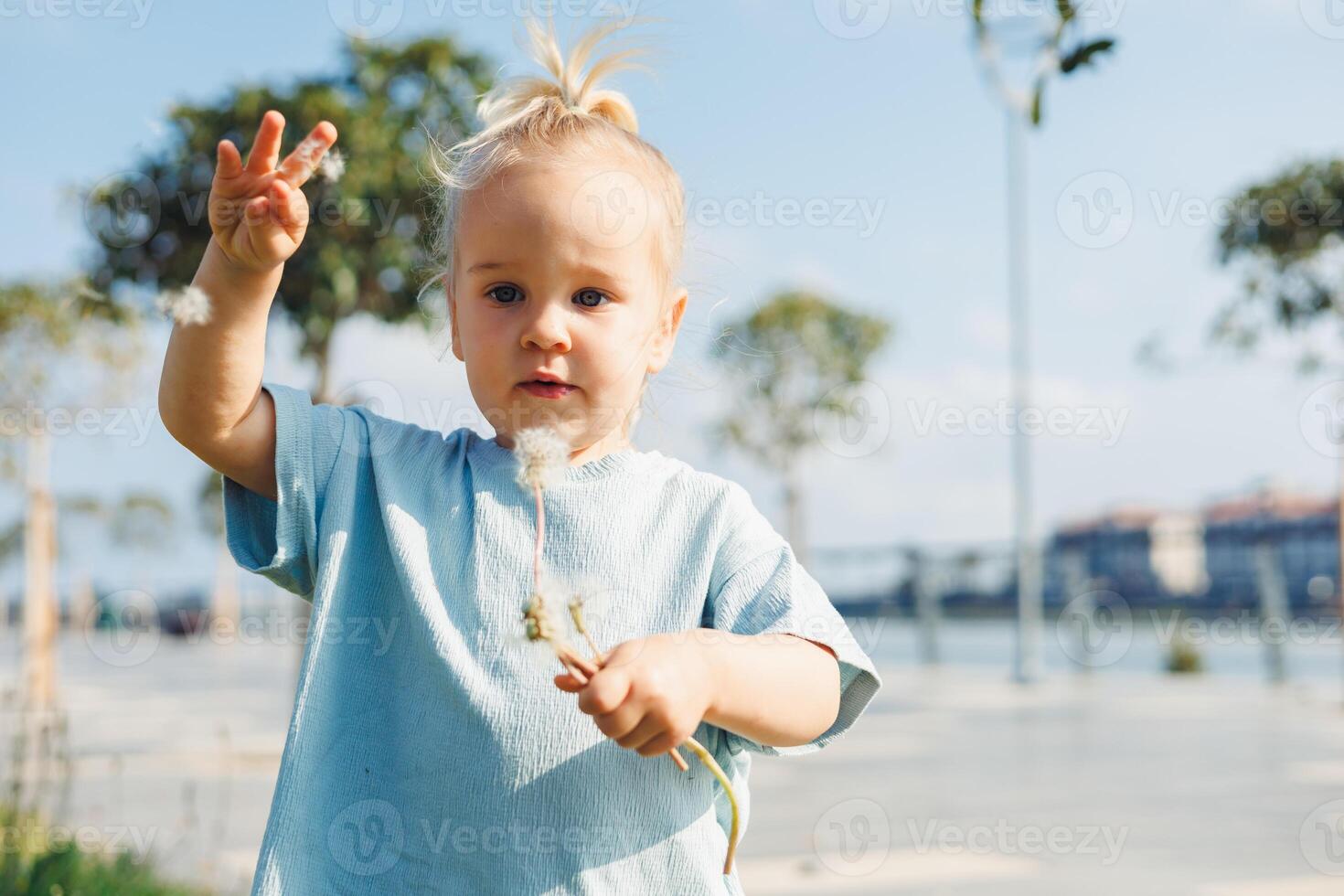 Child enjoys a sunny day outdoors while holding a delicate flower in a scenic park photo