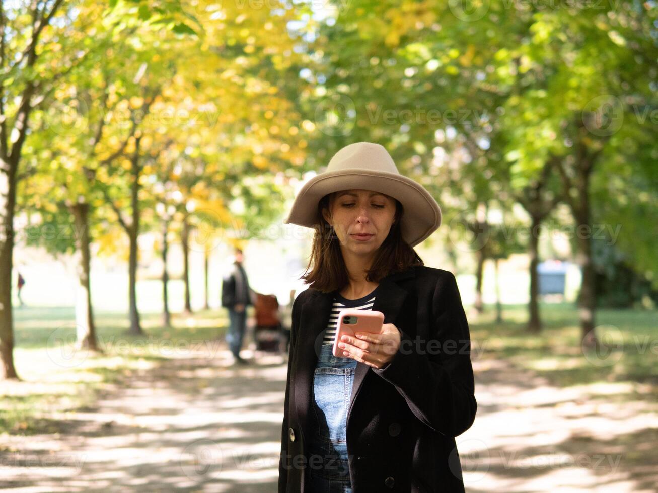 A woman happily enjoys a beautiful day outdoors, focused on her phone amidst the vibrant autumn foliage photo