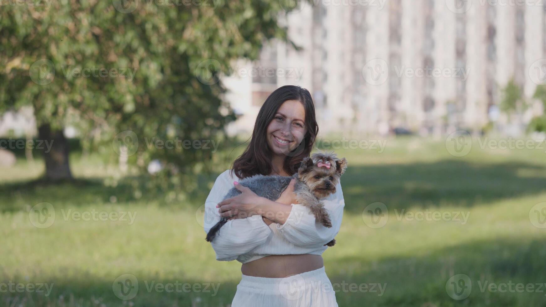 In a vibrant green park setting, a cheerful young woman beams with joy while holding her beloved dog close by photo