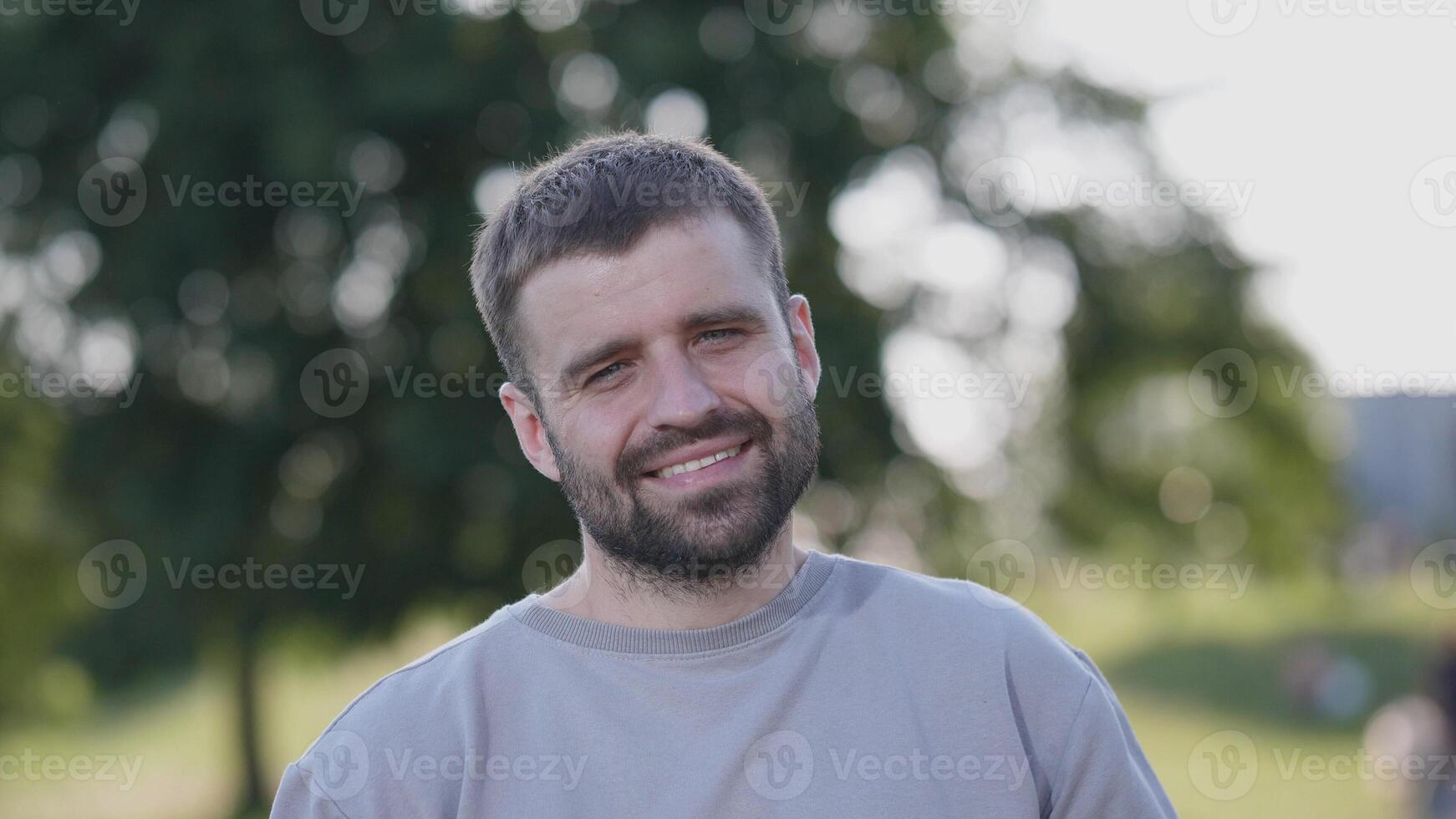 A cheerful young man stands outdoors, enjoying the natural surroundings with a tree in the background. photo