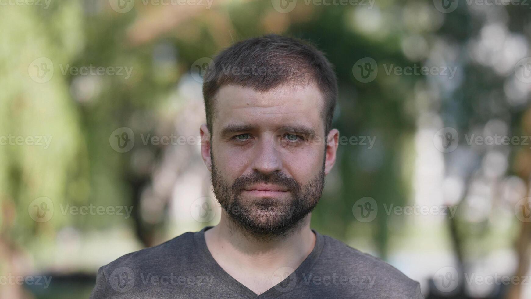 A relaxed portrait showcasing a young man, positioned against a vibrant and lush green background scenery photo
