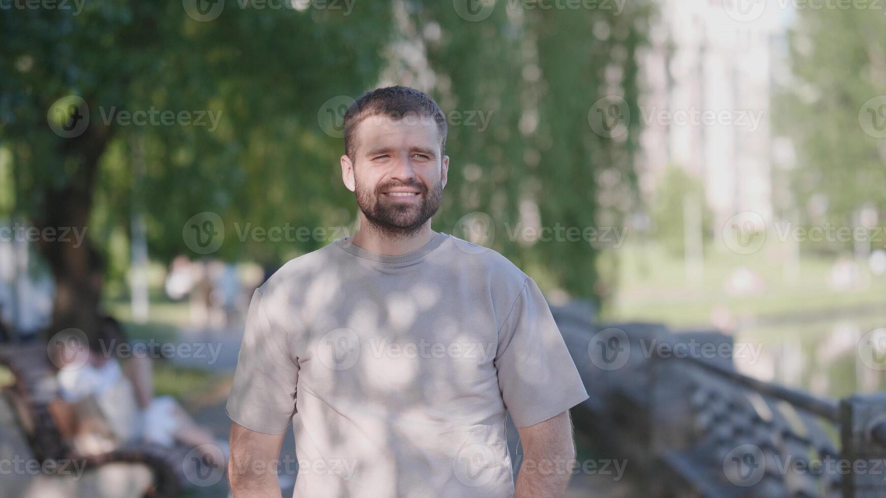 A cheerful man stands in a beautiful park, surrounded by nature and people enjoying their leisure time photo