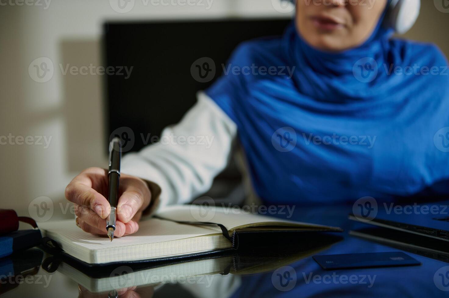 Close-Up of Woman Writing Notes While Listening with Headphones On photo