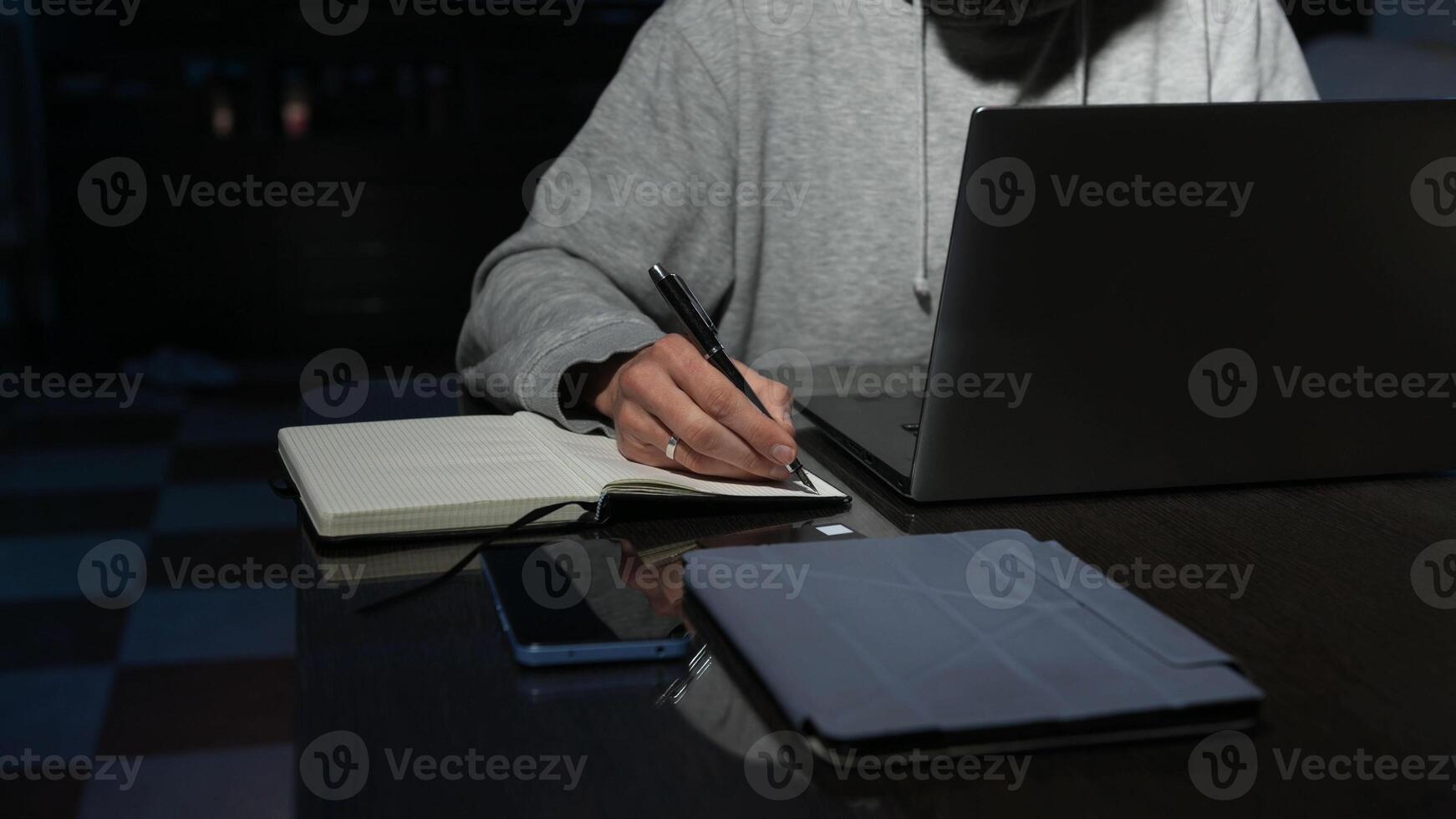 Focused Individual Writing Notes and Using a Laptop at a Desk photo