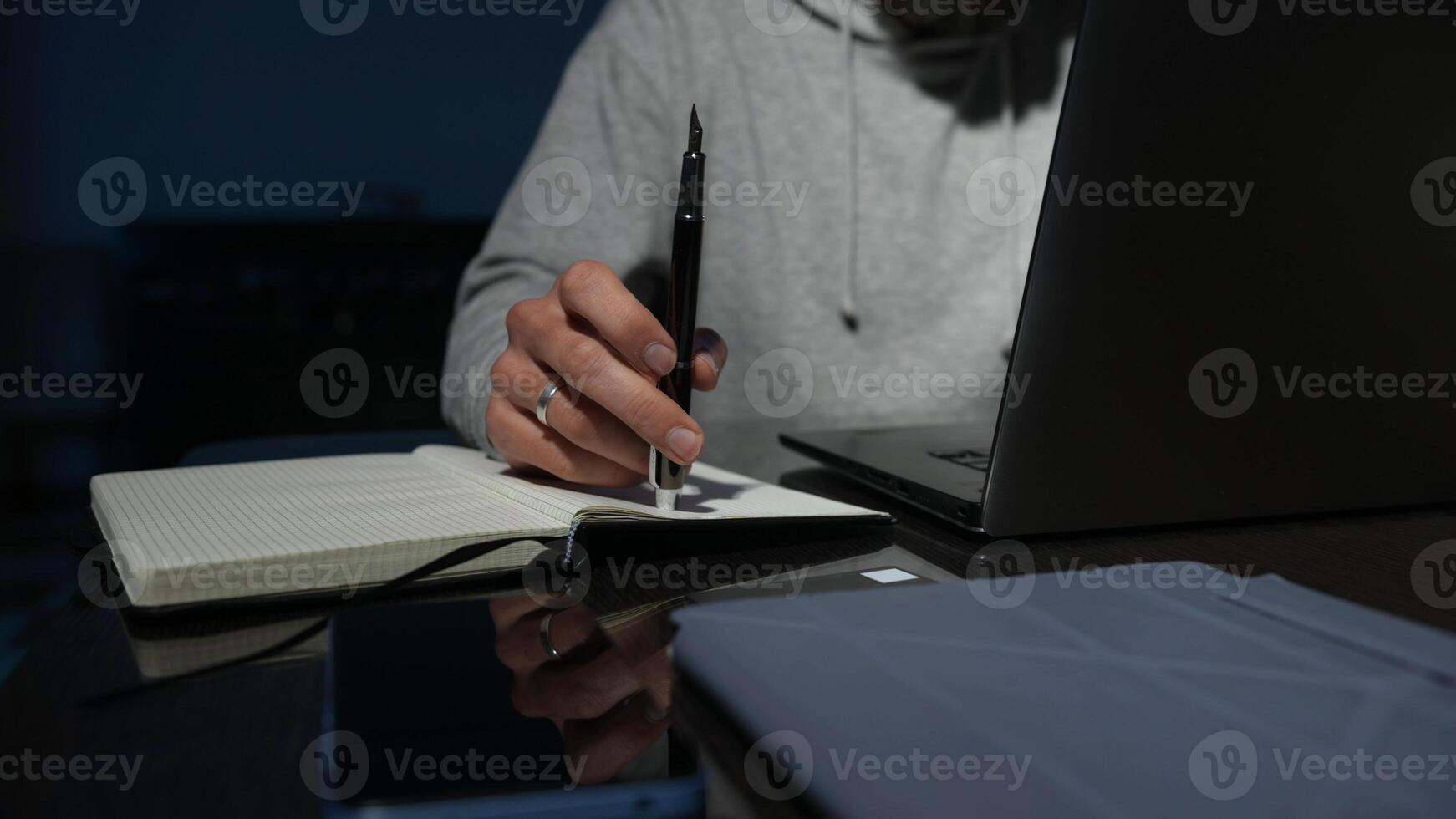 Focused Individual Writing in Notebook with Laptop Under Low Light photo