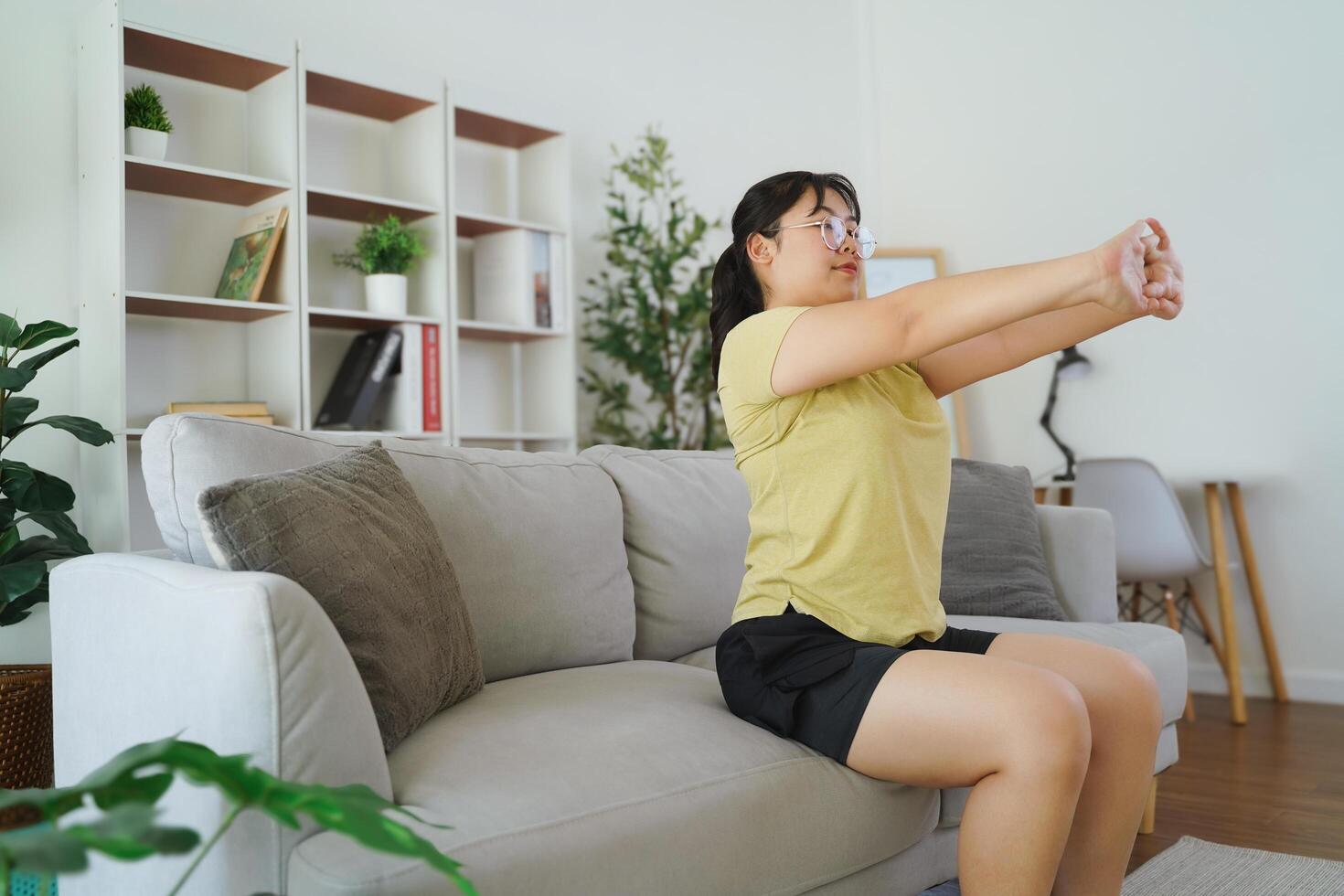 plump Asian woman is stretching while sitting on a sofa in her living room at home. photo