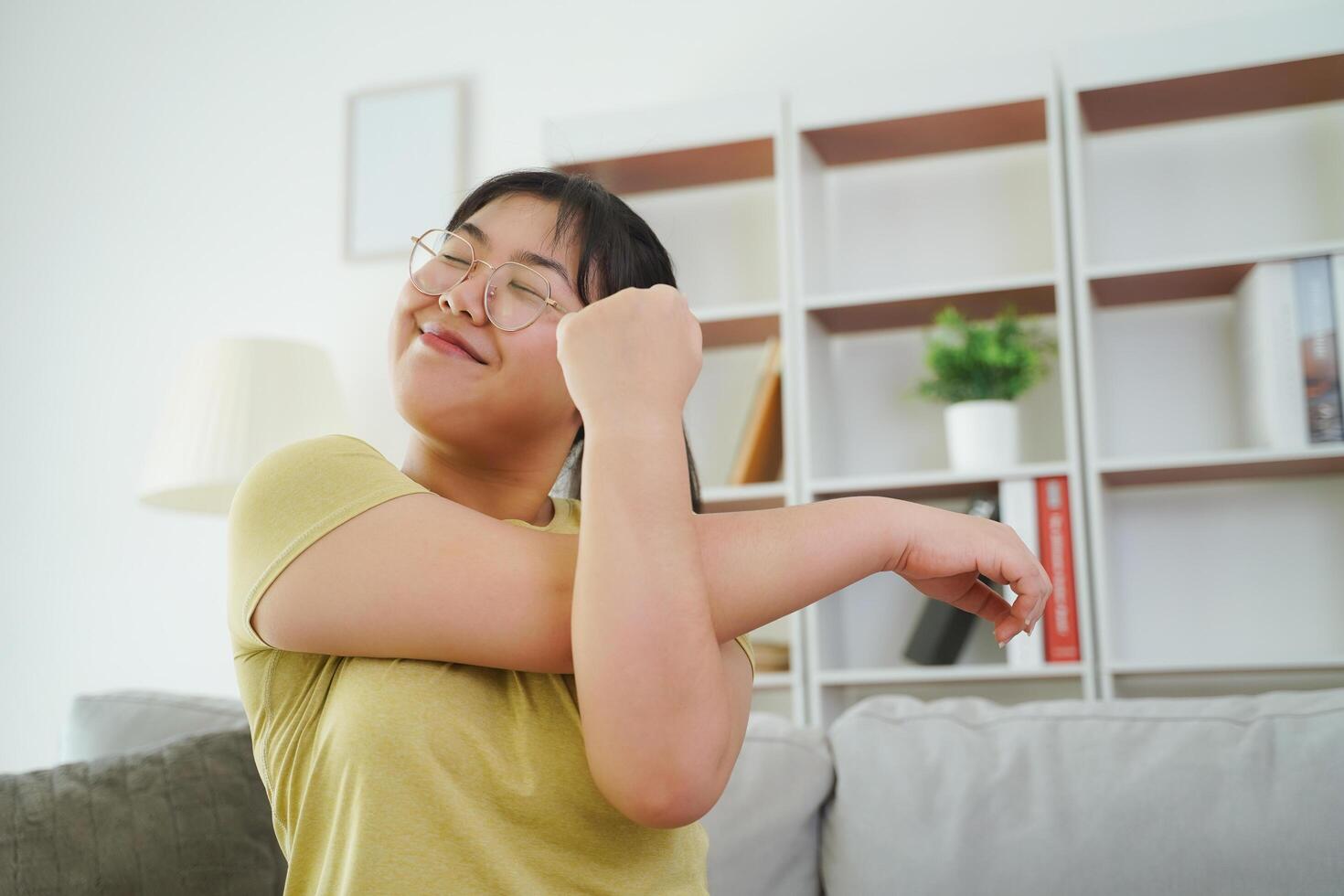 A plump Asian woman stretching her muscles while sitting on a sofa in her living room at home. photo
