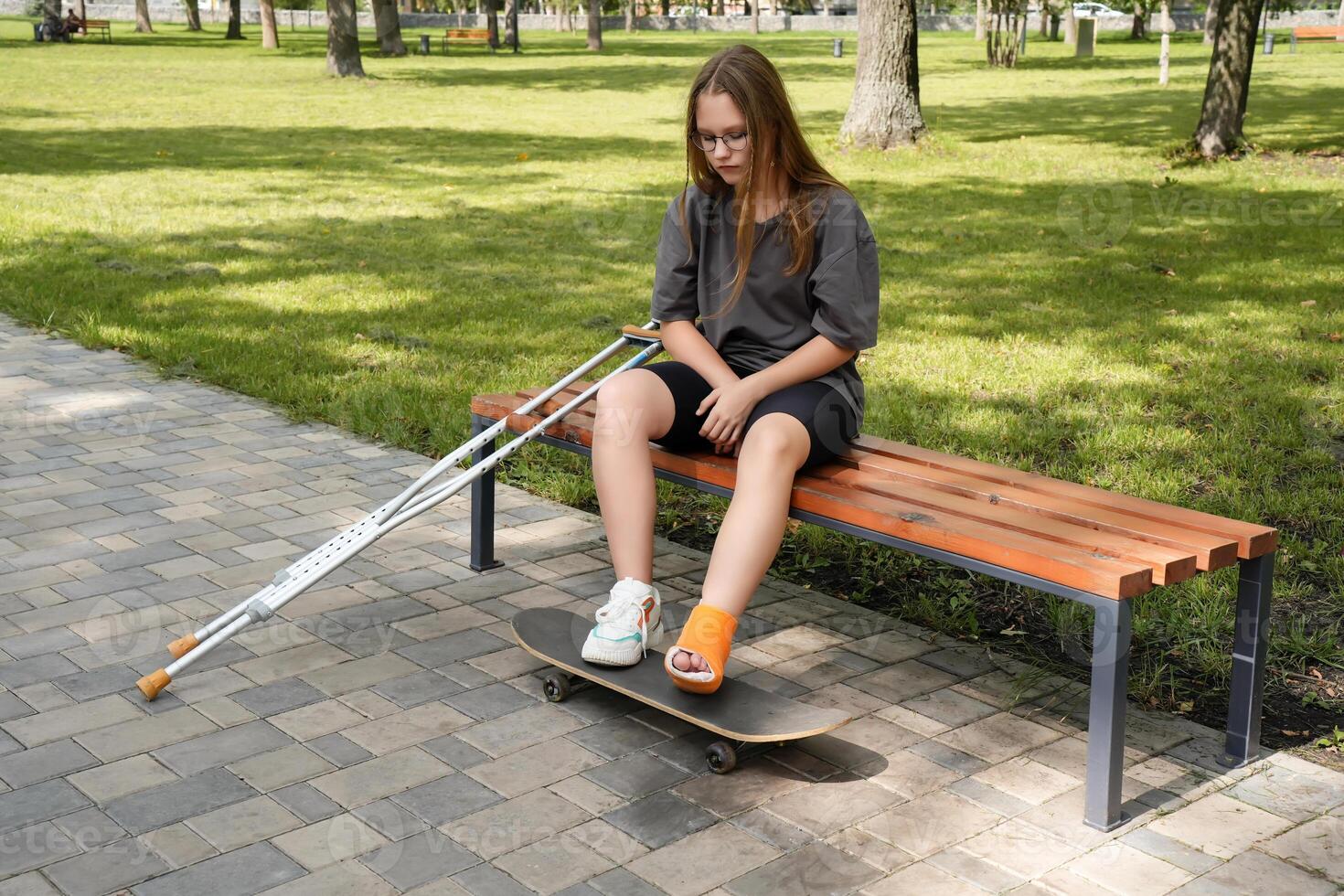 Resting on a park bench, a girl clutches her skateboard, her pensive gaze suggesting an internal struggle with obstacles that test her resilience photo