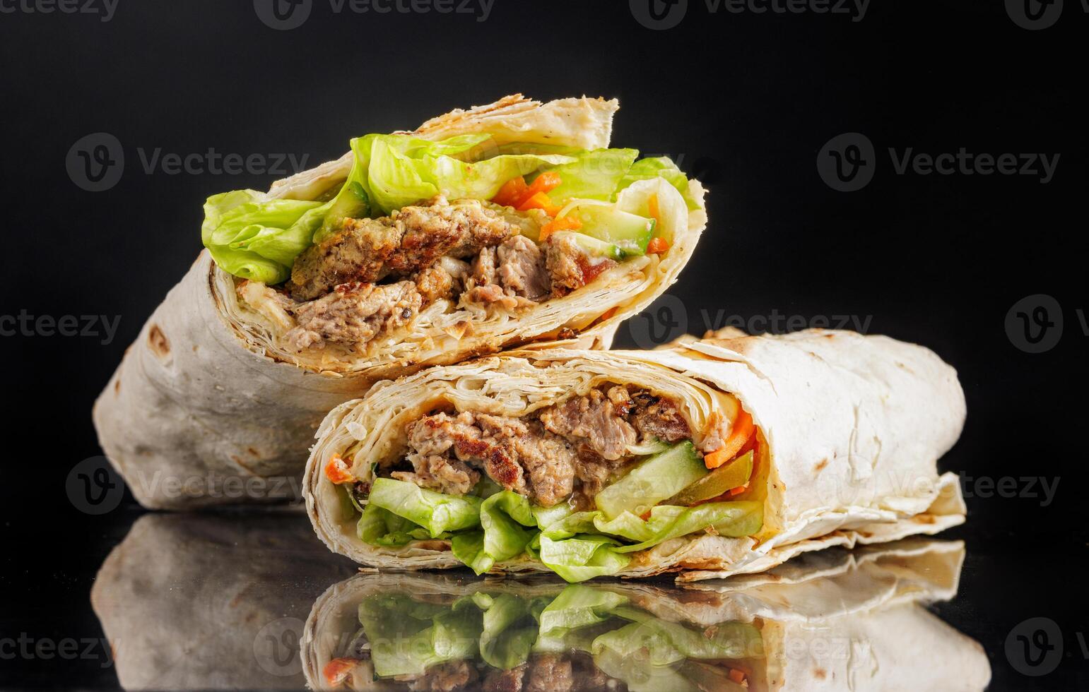 Delicious shawarma wrap with grilled meat, lettuce, vegetables, and sauce on black background. photo