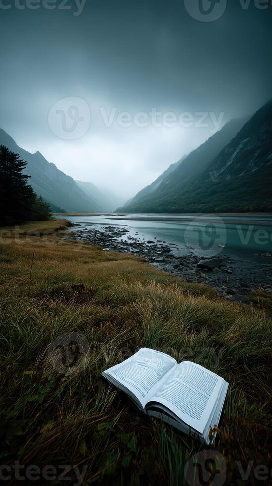 Open book on grass by serene river with misty mountains in background photo
