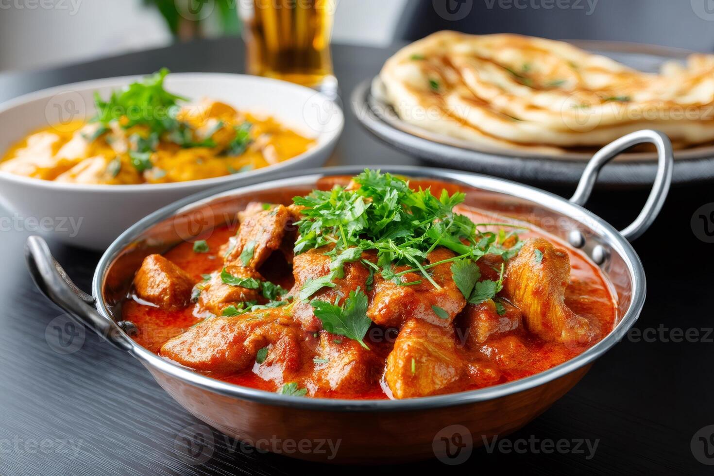 Chicken tikka masala garnished with coriander served with naan bread and another indian sauce photo