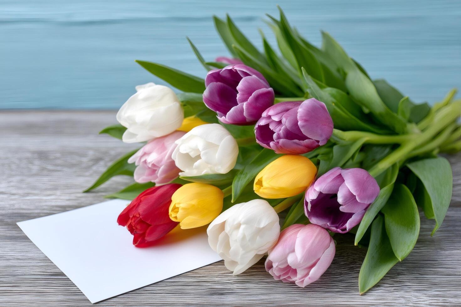 Colorful bouquet of tulips lying on a wooden surface with a blank greeting card photo